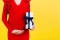 Cropped Image Of Pregnant Woman In Red Dress Holding A Gift Box And Touching Her Belly At Yellow Background. Expecting A Baby Boy