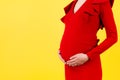 Cropped image of pregnant woman wearing red dress. Young mother is hugging her belly expecting a baby at yellow background. Copy Royalty Free Stock Photo