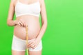 Cropped image of pregnant woman in white underwear measuring her growing abdomen at green background. Inch tape measure. Copy Royalty Free Stock Photo