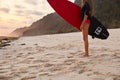 Cropped image of slim female surfer holds surfboard, wears red bikini, stands on sandy beach, ready to hit waves, likes