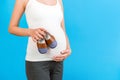 Cropped image of small shoes for a baby boy in pregnant woman`s hands against her abdomen at blue background. Love to the future Royalty Free Stock Photo