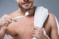 Cropped image of smiling bearded man with towel on shoulder holding toothbrush with toothpaste in hand, Royalty Free Stock Photo