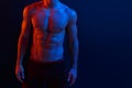 Cropped image of a strong athletic young man model showing six pack abs, over dark neon background. Horizontal shot