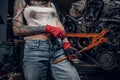 Stylish female model with tattoed body repairs a car engine suspended on a hydraulic hoist in the workshop. Royalty Free Stock Photo