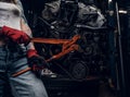 Stylish female model with tattoed body repairs a car engine suspended on a hydraulic hoist in the workshop. Royalty Free Stock Photo