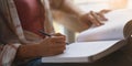 Cropped image of university student tutoring her lesson with book that putting on her lap while sitting at the working desk.