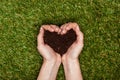 cropped image of woman holding heart shaped soil in hands above green grass, earth Royalty Free Stock Photo