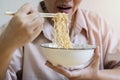 Cropped image of woman isolated on beige background holding a bowl of noodles with chopsticks and eating it Royalty Free Stock Photo