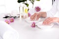 cropped image of woman receiving bath for nails at table with flowers, towels, candles, aroma oil bottles, nail polishes, cream
