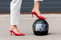 cropped image of woman in red high heels putting leg on motorcycle helmet on street