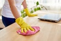 Cropped image of woman`s hand in yellow rubber protective glove cleaning wooden tablel with pink rag, copy space, soft focuse.