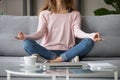 Cropped image woman sitting on couch in lotus pose meditating
