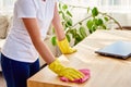 Cropped image of woman in white shirt and yellow protective rubber gloves cleaning at home and wiping dust on wooden tablel. Royalty Free Stock Photo