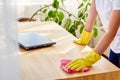 Cropped image of woman in white shirt and yellow protective rubber gloves cleaning at home and wiping dust on wooden tablel. Royalty Free Stock Photo