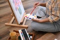 Cropped image of young female artist holding palette and painting picture on canvas with oil paints in home studio Royalty Free Stock Photo