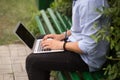 Cropped image of young man sitting at on the bench in the park, using a laptop. Royalty Free Stock Photo