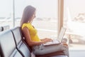 Cropped image of young woman holding a laptop on lap typing keyboard indoors in public place