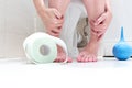 Cropped legs of a woman, sitting on a toilet with lowered panties, blue cleansing enema and a roll of toilet paper in front. Royalty Free Stock Photo