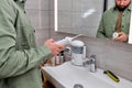 Cropped male casually dressed using oral dental irrigator with in bathroom near mirror