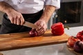 Cropped male chef precisely slicing red onions on wooden cutting board in restaurant kitchen Royalty Free Stock Photo