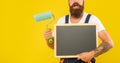 cropped man renovator hold paint roller and blackboard with copy space on yellow background