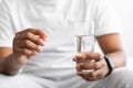 Cropped millennial african american guy in white t-shirt hold pill and glass of water in bedroom