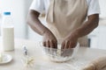 Cropped millennial african american woman in apron making dough on table in kitchen interior, close up