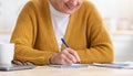 Cropped of old woman sitting in kitchen, taking notes