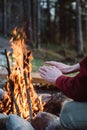 Cropped outdoor image of young man warming his hands by the near bonfire.