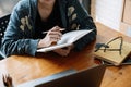 Cropped photo of asian woman writing making list taking notes in notepad working or learning on laptop indoors- Royalty Free Stock Photo