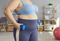 Cropped photo of a belly of fat woman doing sport exercises with dumbbells at home.