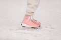 Cropped photo of child girl legs wearing in pink skates and warm clothes at the rink on natural ice on cold winter day