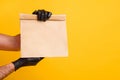 Cropped photo of delivery man arms hold takeout paper package wear black gloves isolated bright yellow color background