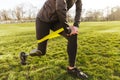 Cropped photo of disabled girl in tracksuit, exercising and doing lunges with prosthetic leg on grass using resistance band Royalty Free Stock Photo