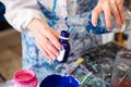 Cropped photo of hands of woman in robe covered with stains pouring water from glass jar into small plastic bottle. Royalty Free Stock Photo