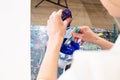 Cropped photo of hands of woman in white robe pouring paint from small plastic bottle into bucket with blue, mixing. Royalty Free Stock Photo