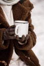 Cropped photo of little girl in warm clothes and mittens holding a big white metal cup of hot drink in hands in snowy Royalty Free Stock Photo