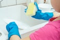 Cropped photo of little girl wearing blue gloves, standing near sink, holding yellow sponge, washing dishes in kitchen. Royalty Free Stock Photo