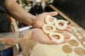 Cropped photo of man holding raw round doughnuts donuts in hands for frying in hot oil in metal pan in kitchen at home.