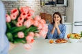 Cropped photo of man's hands holding chic bouquet of pink tulips, happy woman is on blurred background
