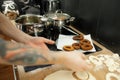 Cropped photo of man taking raw yeast doughnuts donuts for frying in hot oil in metal pan near skimmer on black cooker.