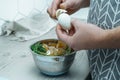 Cropped photo of man wearing apron peeling hardboiled egg over metal bowl full of carrot peelings, standing in kitchen.