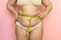 Cropped photo of naked fat and overweight woman tummy, trying to lose weight. Measuring by roulette tape belly. Closeup