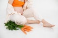 Cropped photo of pregnant woman sitting with bundle of orange vegetables, green carrots. Fresh food nutrition diet