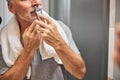 Elderly man with a nose hair trimmer standing near mirror