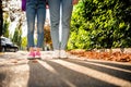 Cropped photo of two girls legs denim jeans sneakers shadow road fallen leaves green park bushes outside Royalty Free Stock Photo