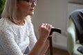 Cropped upset mature woman in glasses holding cane, sitting alone