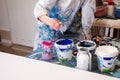 Cropped photo of woman artist in white robe covered with various stains pouring from plastic bottle blue paint in bucket Royalty Free Stock Photo