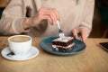 Cropped photo of woman hands in coffee shop cafe, eating tasty brownie powdered sugar. Cup of coffee on wooden table. Royalty Free Stock Photo