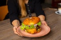 Cropped photo of woman holding plate with burger with lettuce, red onion, cucumbers, fried chicken punctured with knife